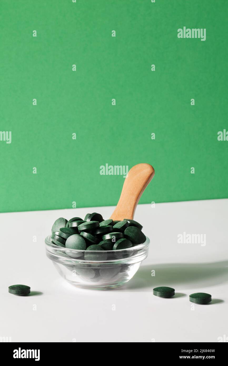 Natürliche Zusatzstoffe und Superfood. Grüne Spirulina-Algenpillen in Schüssel mit Löffel auf grünem, weißem Hintergrund. Gesunde concept.organic Lebensmittel kopieren Raum Stockfoto