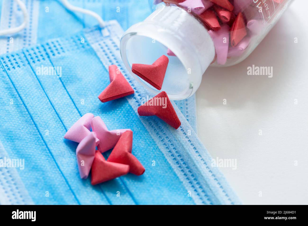 Blaue Einweg-Masken, Rosa und rot dreidimensionale Origami-Kunstwerk und transparentes Glas - Stock Foto Stockfoto