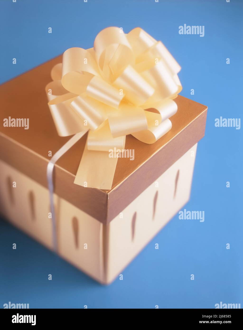 Goldfarbene Geschenkbox mit Band isoliert auf blauem Hintergrund Stockfoto