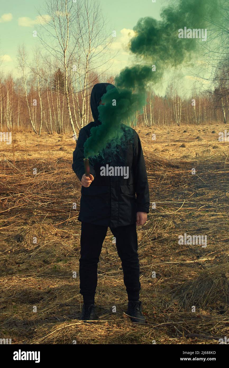 Ein Teenager in einer schwarzen Jacke und einer Maske hält eine grüne Rauchbombe Stockfoto