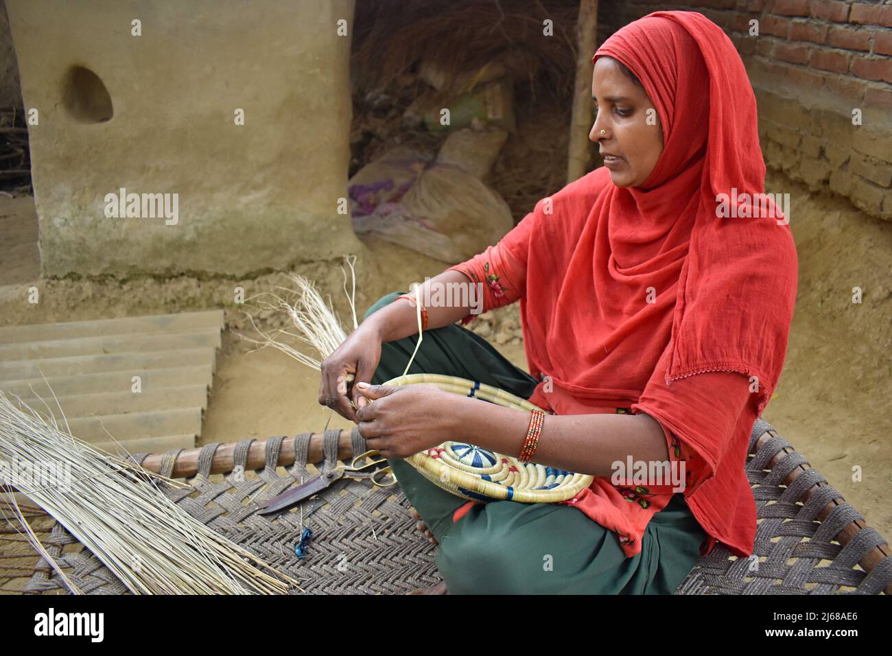 INDIEN, UTTAR PRADESH, Dezember 2021, Eine Frau, die Trockengras Basket macht und auf einem hölzernen Khaiya-Cot im Dorf Amehti sitzt Stockfoto