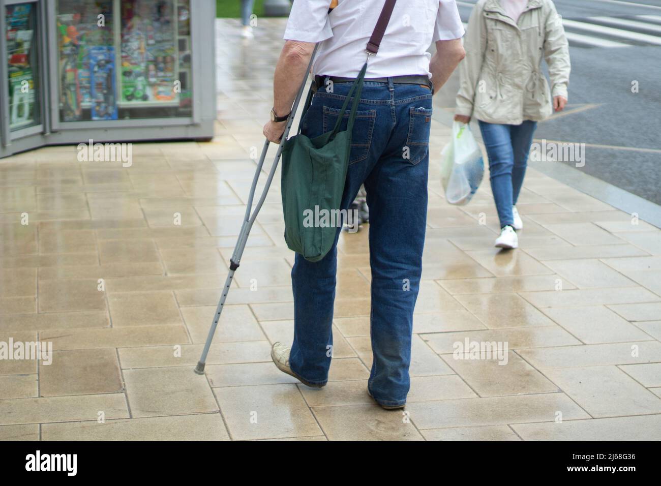 Ein Mann mit einer Krücke in der Stadt. Ein behinderter Mann geht die Straße hinunter. Der Typ mit dem verletzten Bein. Stockfoto