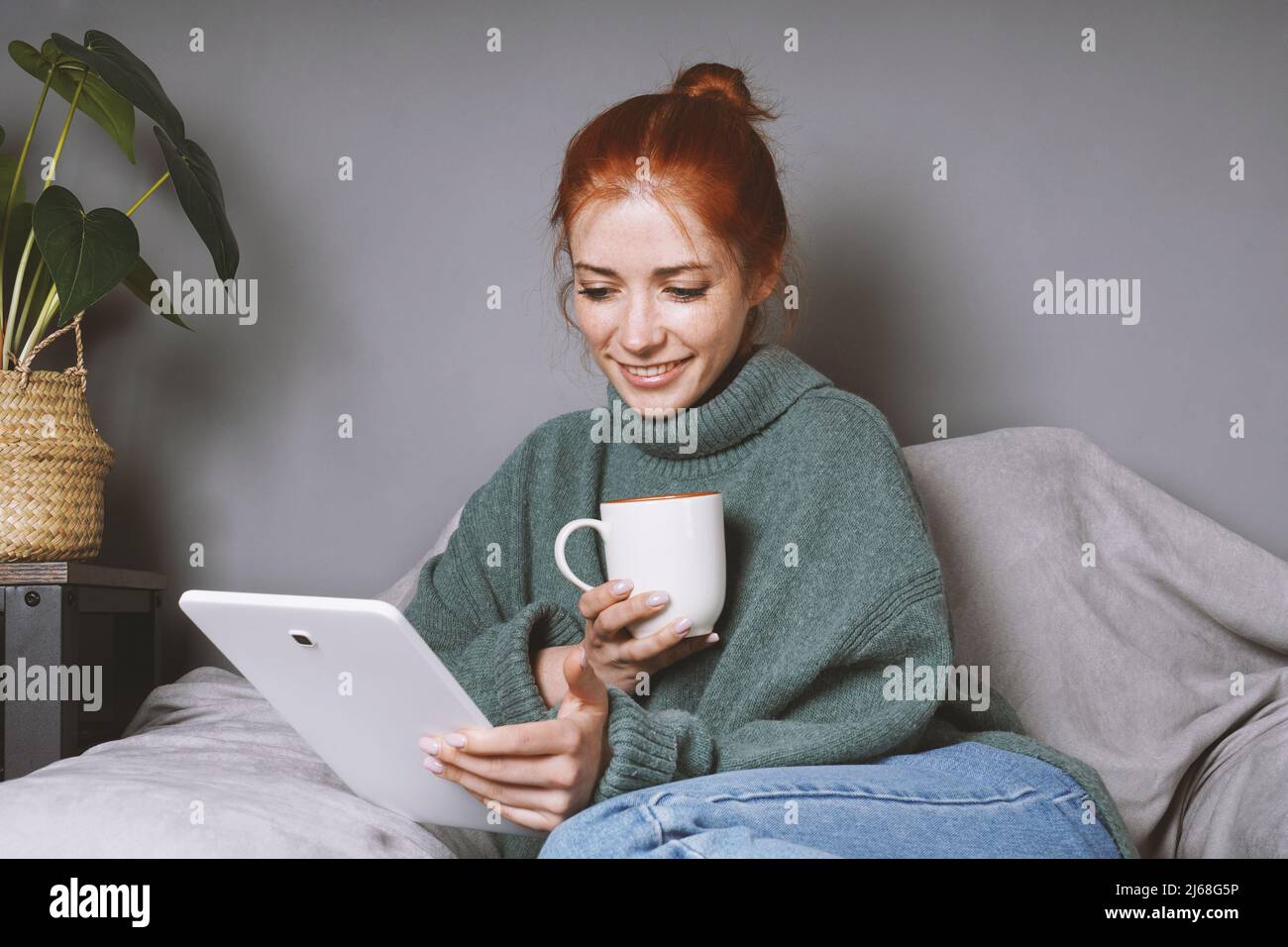Frau, die sich zu Hause mit einem Tablet-Computer zur Unterhaltung oder Kommunikation entspannt und Kaffee trinkt Stockfoto