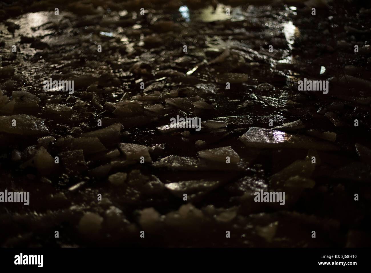 Textur von Eis im Dunkeln. Gebrochenes Eis. Pfütze in der Nacht. Blick auf die Oberfläche von gefrorenem Wasser. Stockfoto