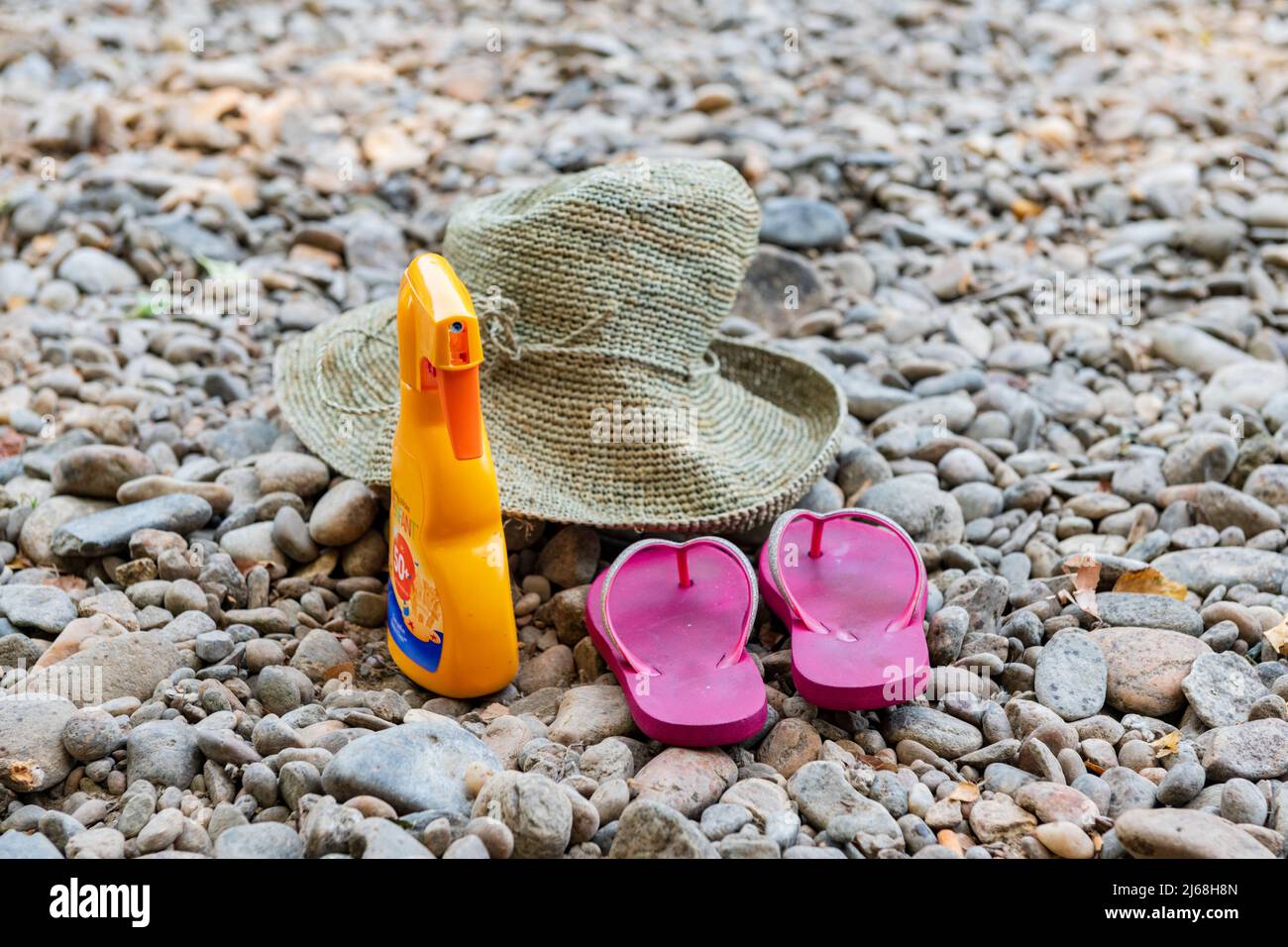 Sonnencreme, Strohhut und Flip-Flops an einem Kieselstrand Stockfoto
