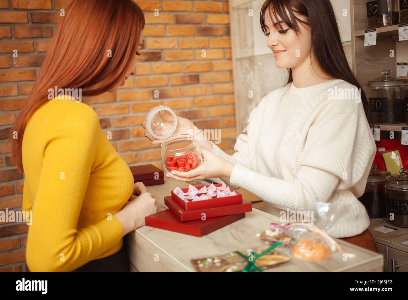 Frau wählt Geschenk zum Valentinstag, schöner Tee in roter Verpackung. Tee-Shop, Verkäufer bietet Waren. Chinesischer Pu-erh-Tee Stockfoto