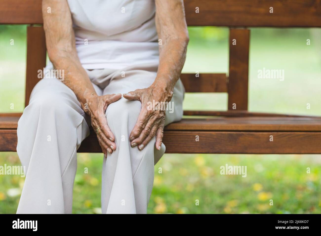 Ältere Frau sitzt auf der Bank und hält ihr schmerzhaftes Knie Stockfoto