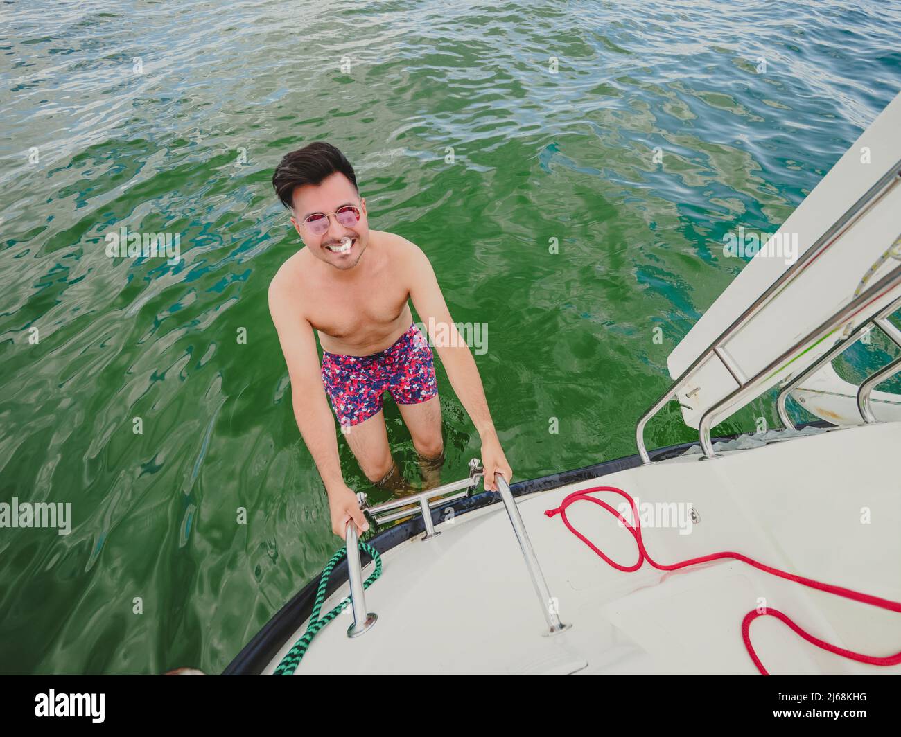 Glücklicher schwarzer Haarmann die Leiter hinunter ins Wasser. Ein Mann auf einer eisernen Leiter auf der Segelyacht A ins Wasser, um zu schwimmen Stockfoto