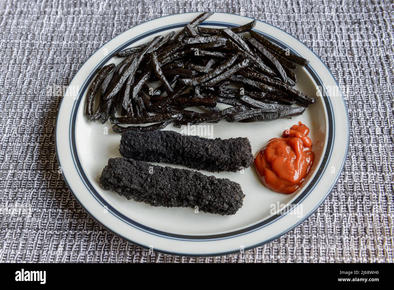 Ein Teller mit stark verbrannten, schwarzen, Fischfingern und Pommes Frites. Stockfoto