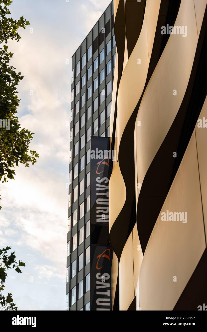 Moderne Fassaden in der Stadt mit dem Saturn-Logo. Banner eines Elektronikladens auf einem geschwungenen Gebäude. Branding und Werbung eines Unternehmens in Deutschland Stockfoto