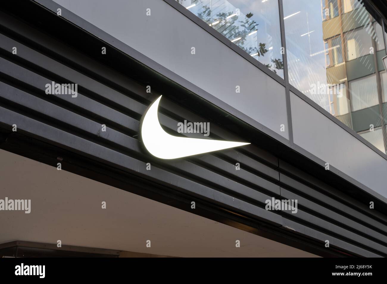 Nike Swoosh Logo an der Fassade eines Geschäfts in der Hauptstadt Deutschlands. Beleuchtetes Firmenmarkenschild als Werbung auf einem Gebäude. Moderne Architektur Stockfoto