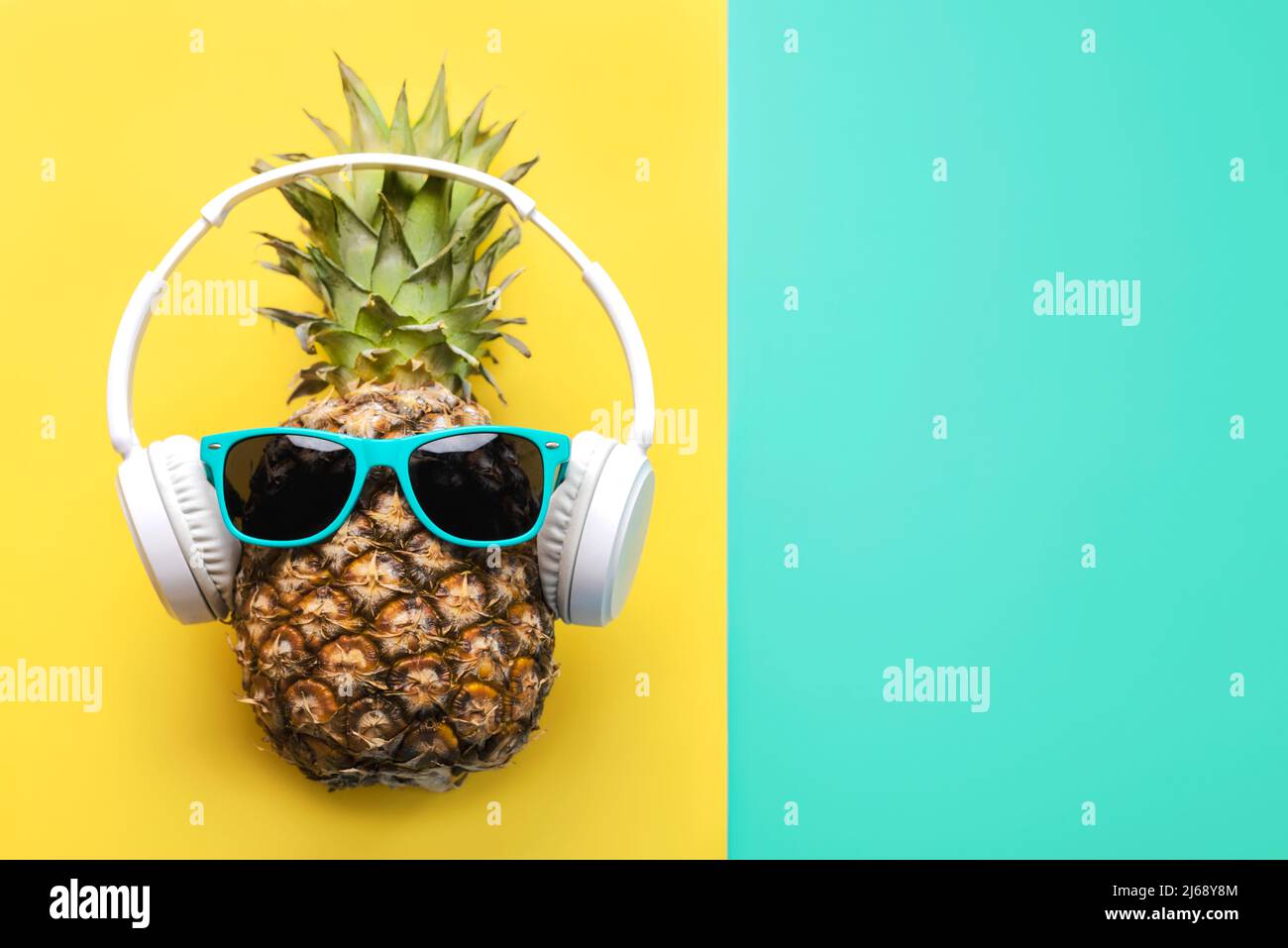 Sommerzeitkonzept. Ananas mit blauer Sonnenbrille, Kopfhörern und Platz für Text auf gelbem und blauem Hintergrund Stockfoto