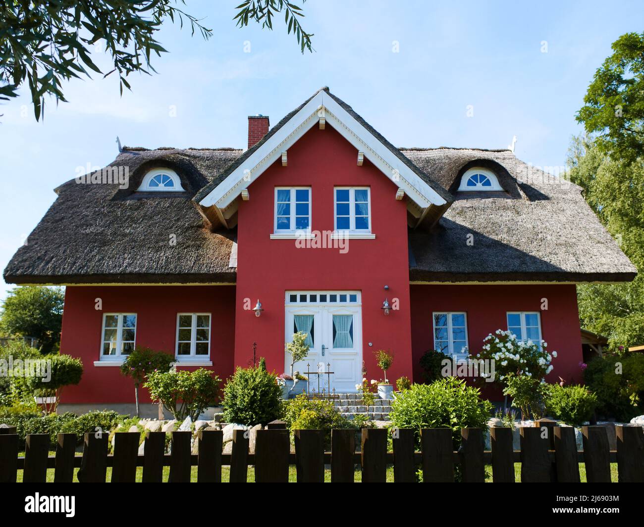 Rotes Haus mit Strohdach in wunderschöner Natur. Grünes Gras und Bäume in einem Grundstück. Traditionelle Immobilien in Europa an einem sonnigen Sommertag. Stockfoto