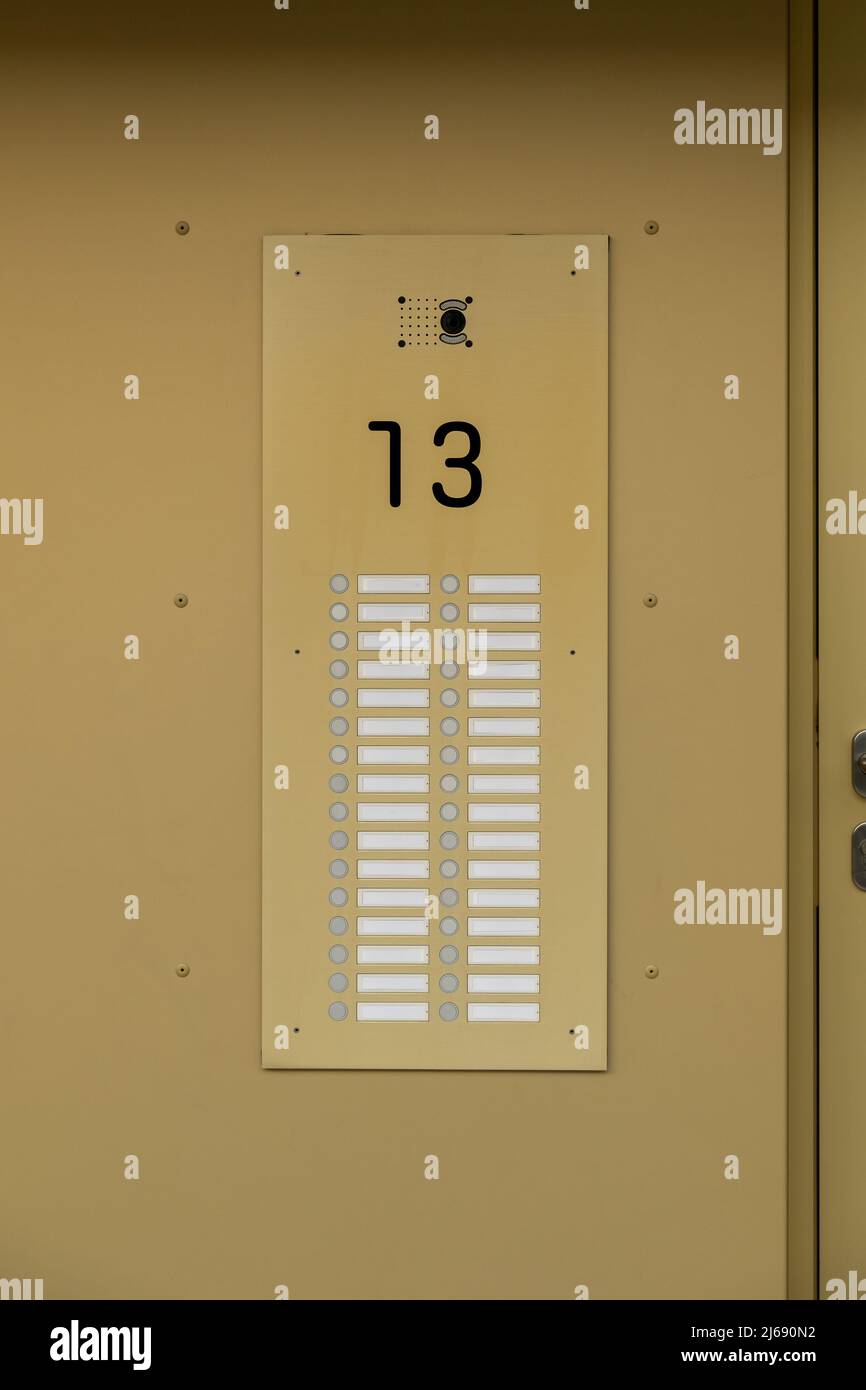 Klingel mit einer großen leeren Türklingel für 32 Wohnungen. Messinggoldfarbene Wand mit Nummer 13 und unbeschriftete Namensschilder für ein Modell. Stockfoto
