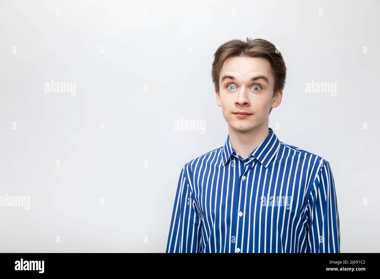 Porträt eines schockierten, staunenden jungen Mannes, der ein blau-weiß gestreiftes Knopfhemd mit weit geöffneten Augen trägt. Studio auf grauem Hintergrund aufgenommen Stockfoto