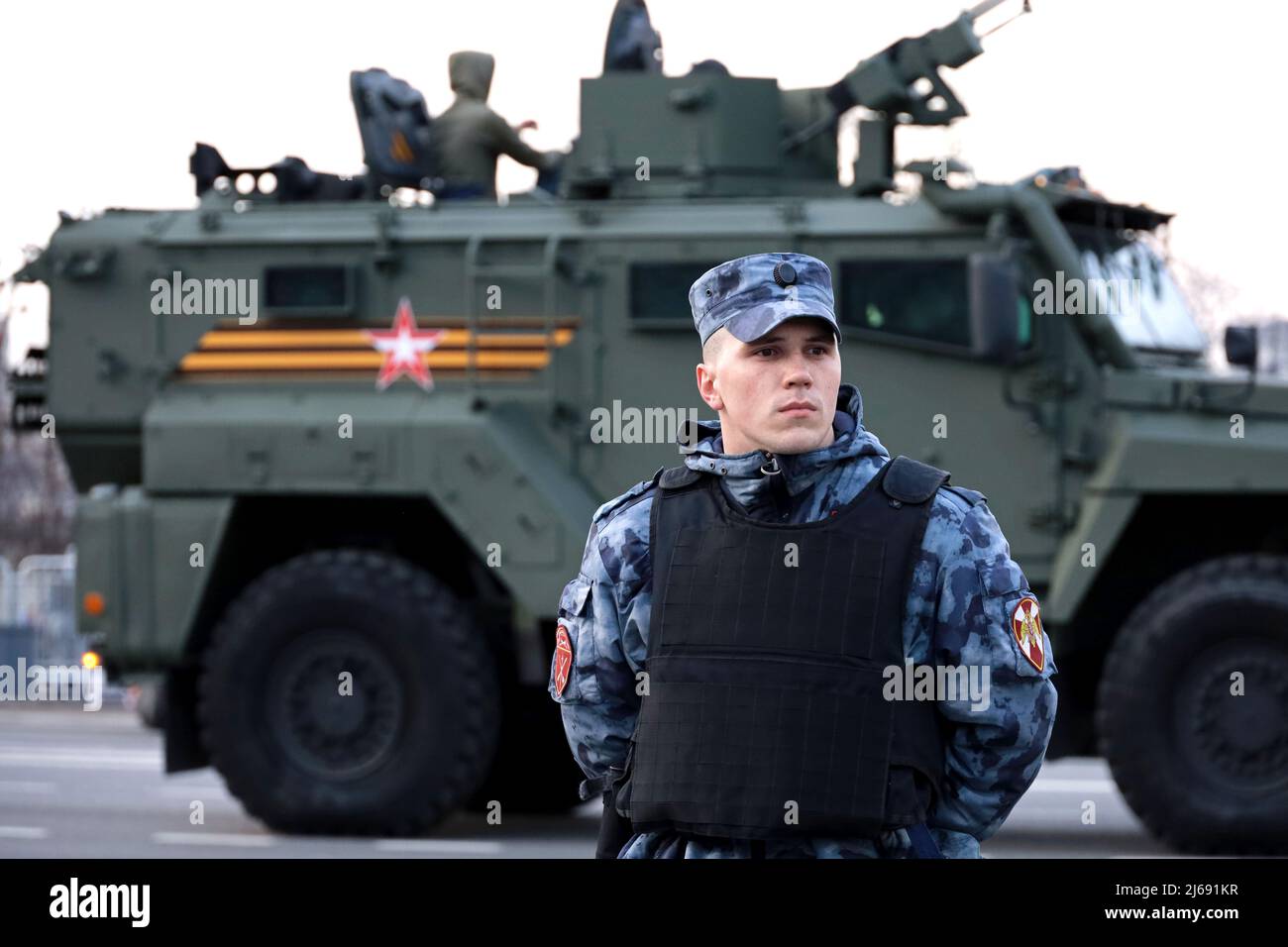 Soldat der russischen Streitkräfte der Nationalgarde in kugelsicherer Weste, die auf dem Hintergrund des gepanzerten Fahrzeugs steht Stockfoto