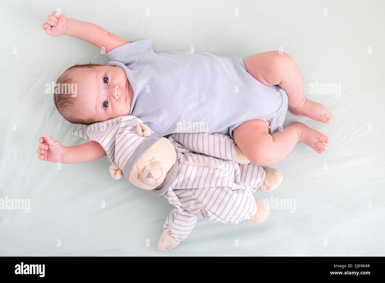 Neugeborener Junge 3 Monate alt liegt in Krippe Kinderkrippe mit blauer Kleidung auf dem Rücken mit Teddybär, schaut auf die Kamera, Baby-Produkte-Konzept, Mock up. Stockfoto
