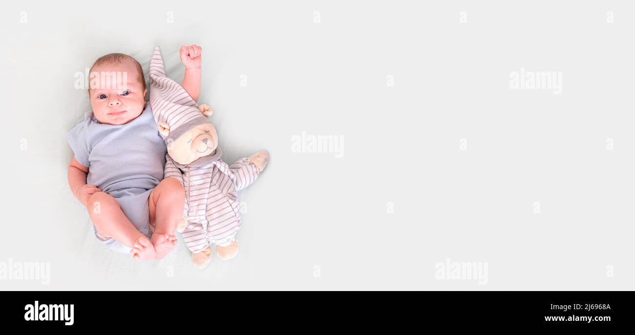Banner neugeborener Junge 3 Monate alt liegt in blauer Kleidung auf dem Rücken mit Teddybär, schaut auf die Kamera, Baby-Produkte-Konzept, Mock-up, Copyspace. Stockfoto