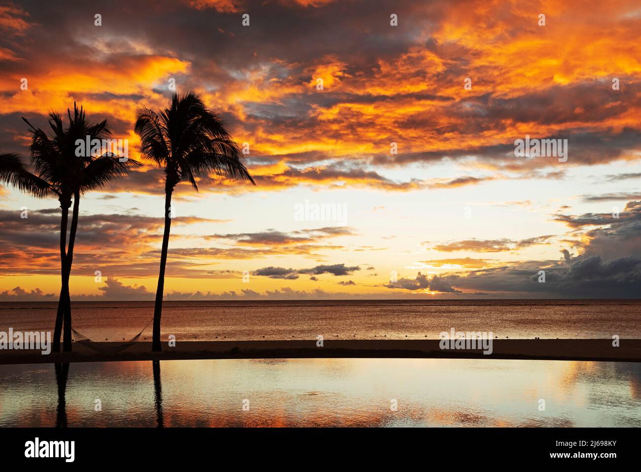 Palmen, die vor roten Wolken geschildet sind, spiegeln sich in einem unendlichen Pool während des Sonnenuntergangs über einem Strand in Flic en Flac, Mauritius, Indischer Ozean, Afrika Stockfoto Palmen, die vor roten Wolken geschildet sind, spiegeln sich in einem unendlichen Pool während des Sonnenuntergangs über einem Strand in Flic en Flac, Mauritius, Indischer Ozean, Afrika Stockfoto