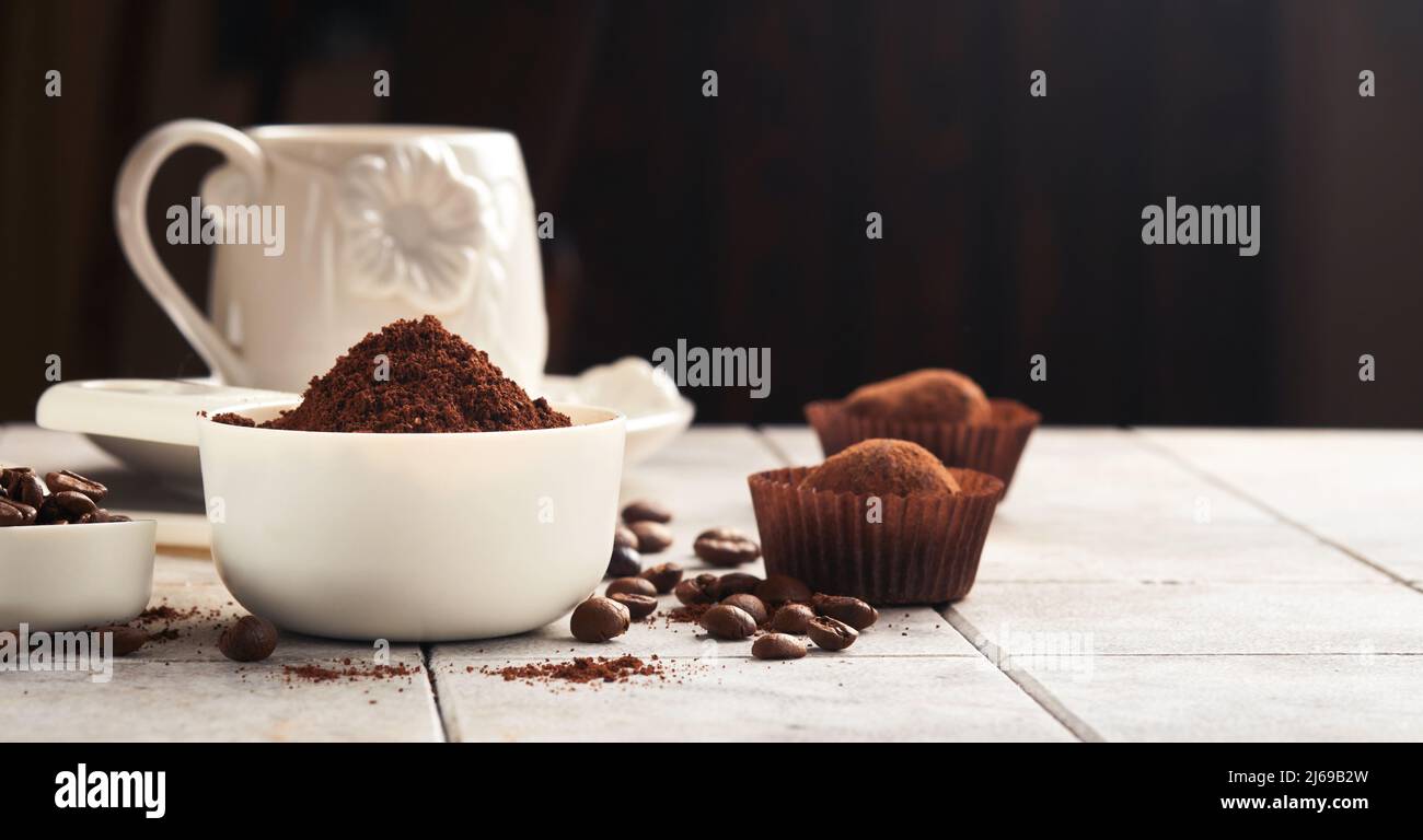 Hintergrund für Kaffee. Messlöffel mit gemahlenem Kaffee, Bohnen, Tasse und süßen Schokoladentrüffeln auf alten Kacheln geknackt Tischhintergrund. Hintergrund der Speisen. Stockfoto