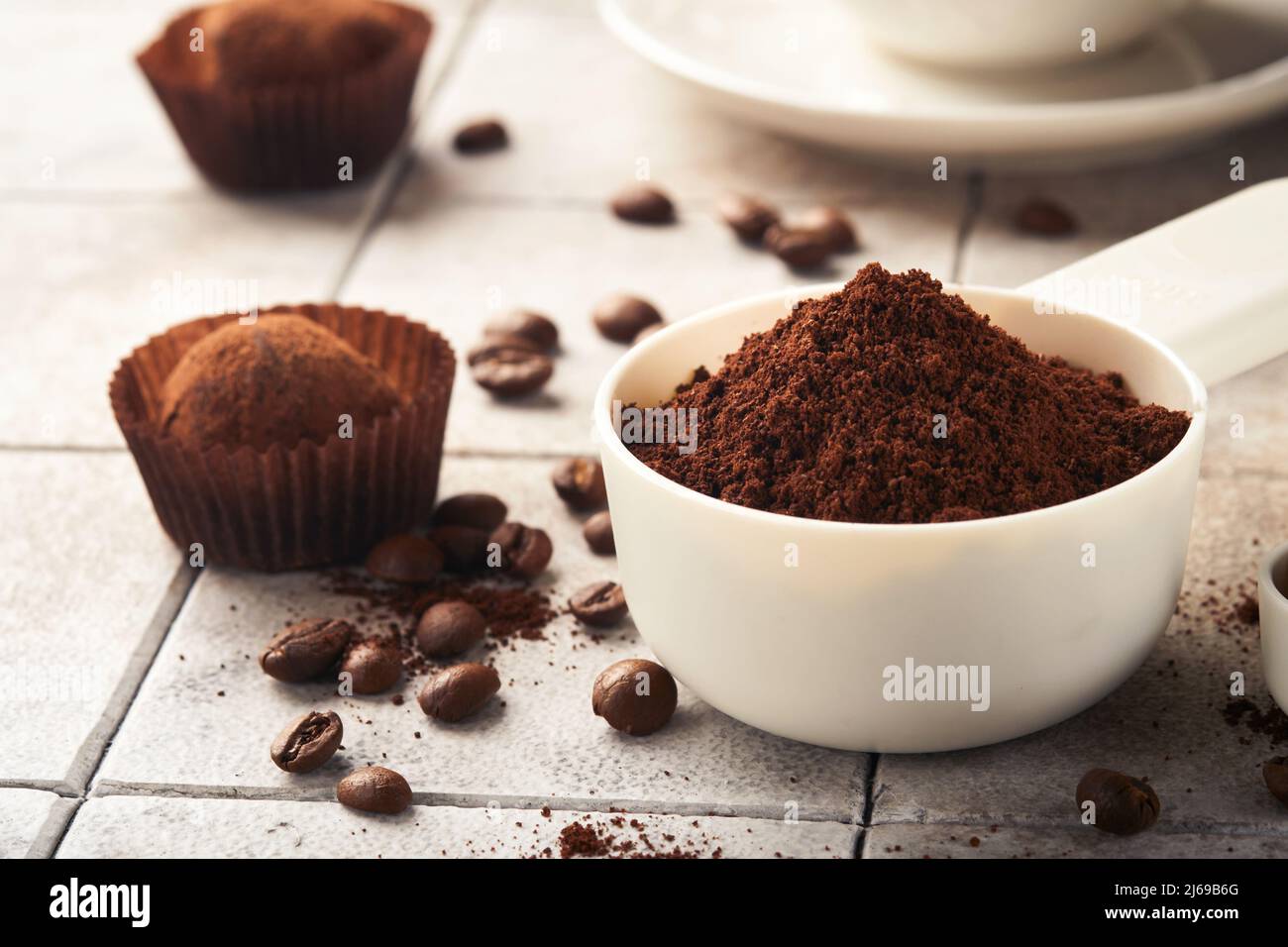 Hintergrund für Kaffee. Messlöffel mit gemahlenem Kaffee, Bohnen, Tasse und süßen Schokoladentrüffeln auf alten Kacheln geknackt Tischhintergrund. Hintergrund der Speisen. Stockfoto