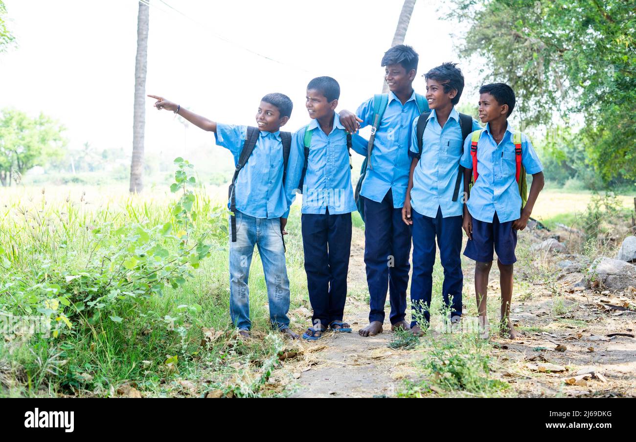 Dorfgruppe von Kindern in Uniform mit Laptop, während sie in der Nähe von Reisfeld sitzen - Konzept der Bildung, Entwicklung und Technologie. Stockfoto