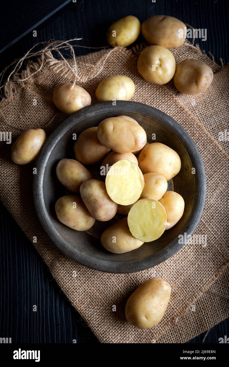 Rohe neue Kartoffeln in einem rustikalen Gericht auf einem dunklen Holztisch. Stockfoto
