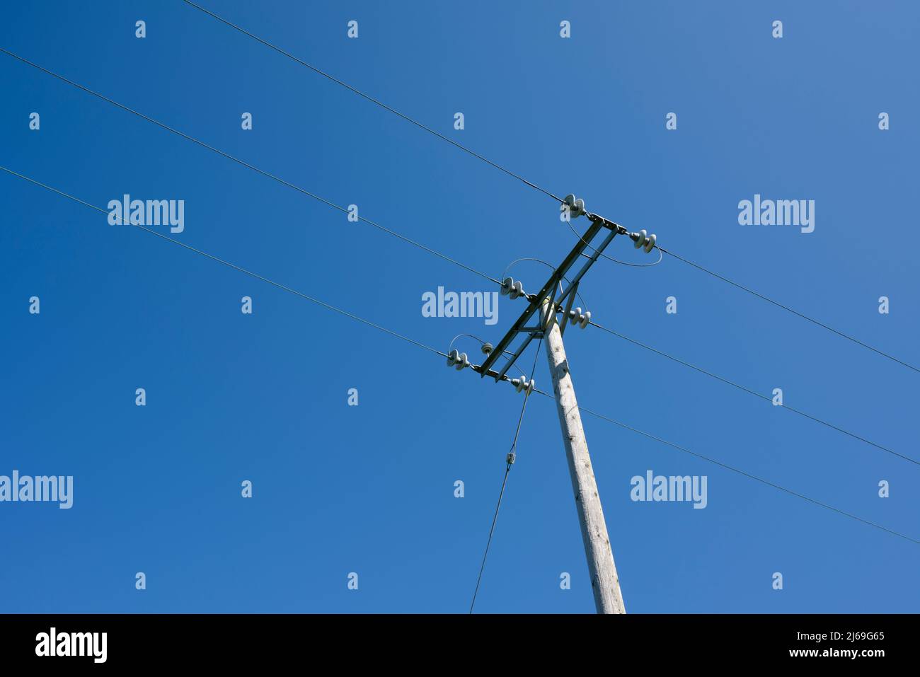 11kV dreiphasige Hochspannungsstromverteilerkabel mit Holzmast an einem klaren blauen Himmel in Somerset, England. Stockfoto