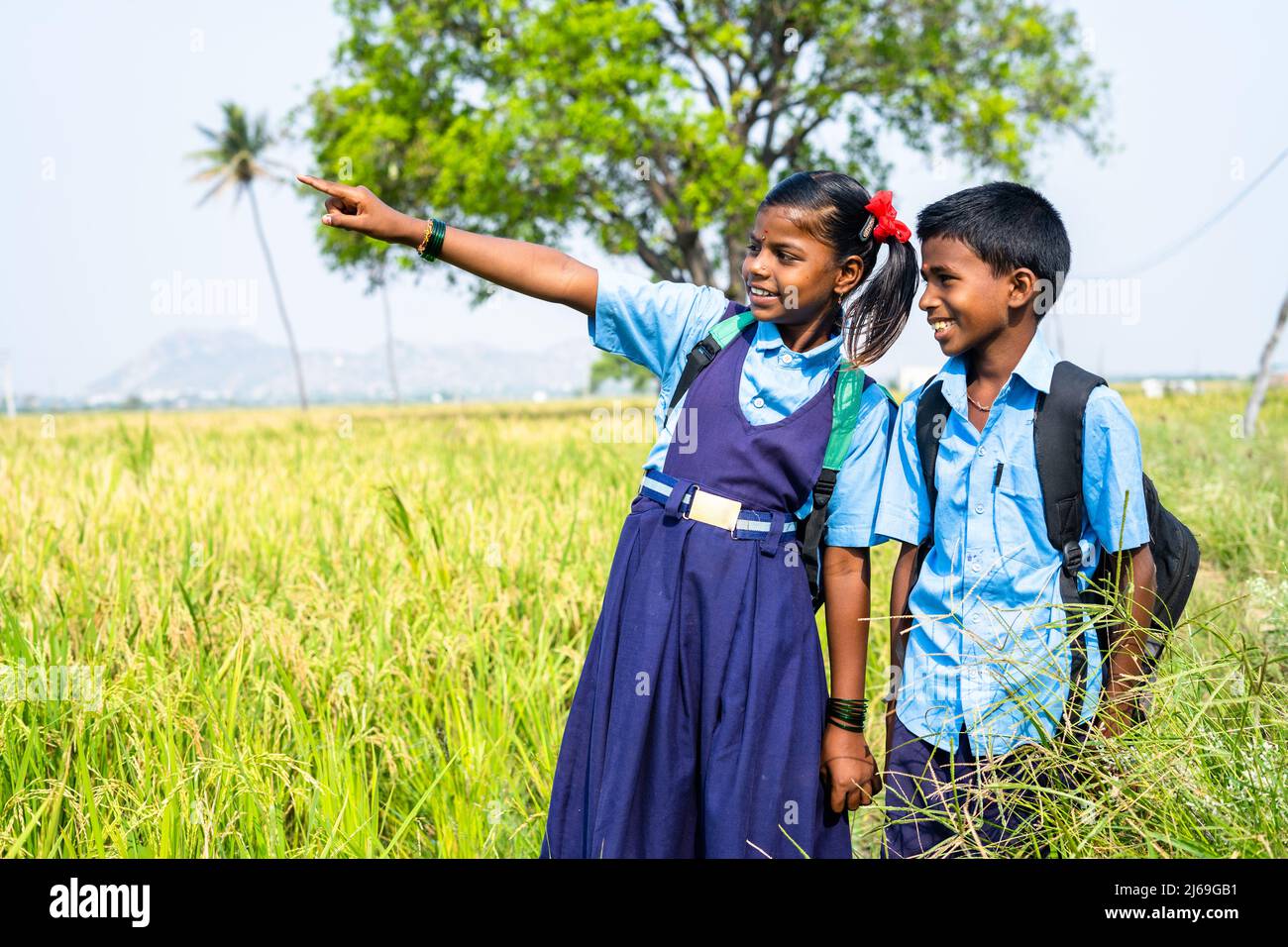 Teenager-Geschwister mit Schulkleidung gehen auf Reisfeld zur Schule und schauen sich die Natur an - Konzept von Bildung, Armut, Dorfleben Stockfoto