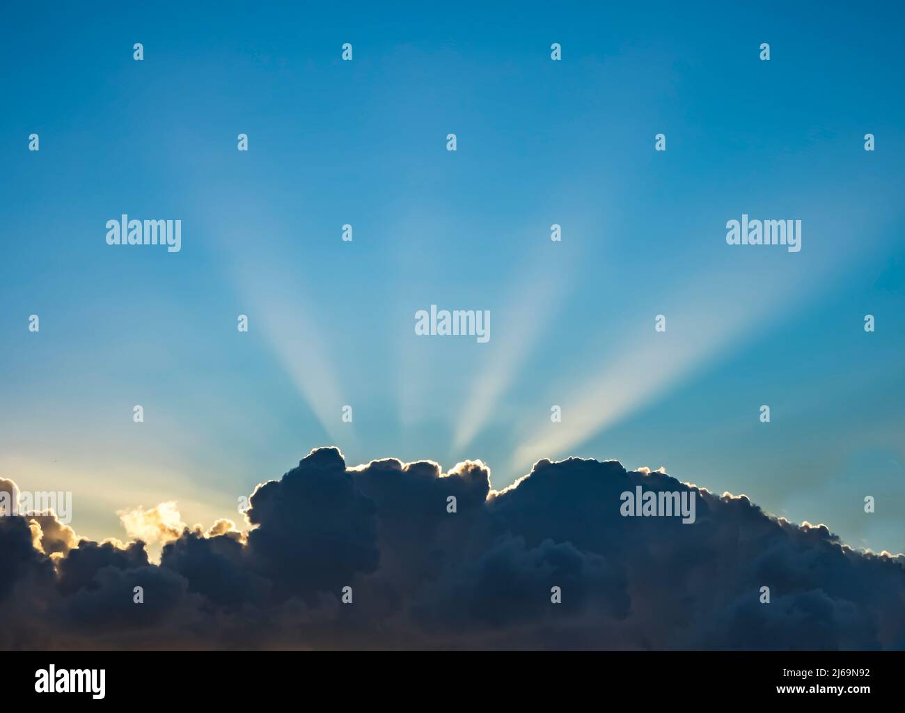 Sonnenstrahlen hinter Wolken am blauen Himmel Stockfoto