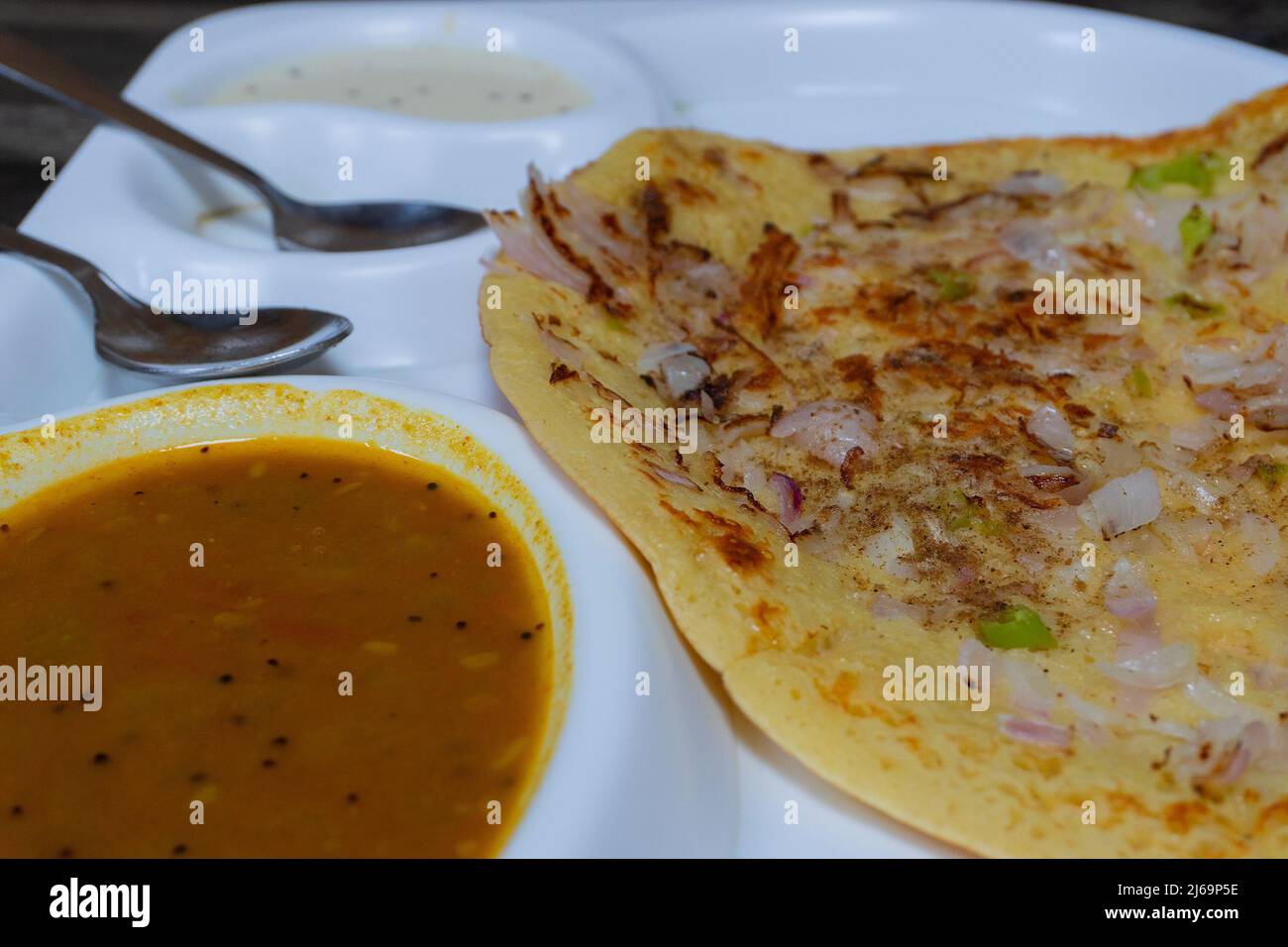 Uttapam wird mit Chutney auf einem weißen Teller serviert, einem indischen Gemüsegericht. Stockfoto