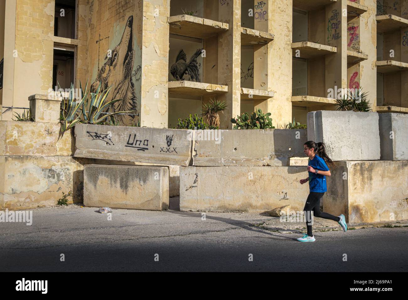 Eine Frau, die am verlassenen Jerma Palace Hotel, Marsaskala, Malta, vorbeijoggt Stockfoto