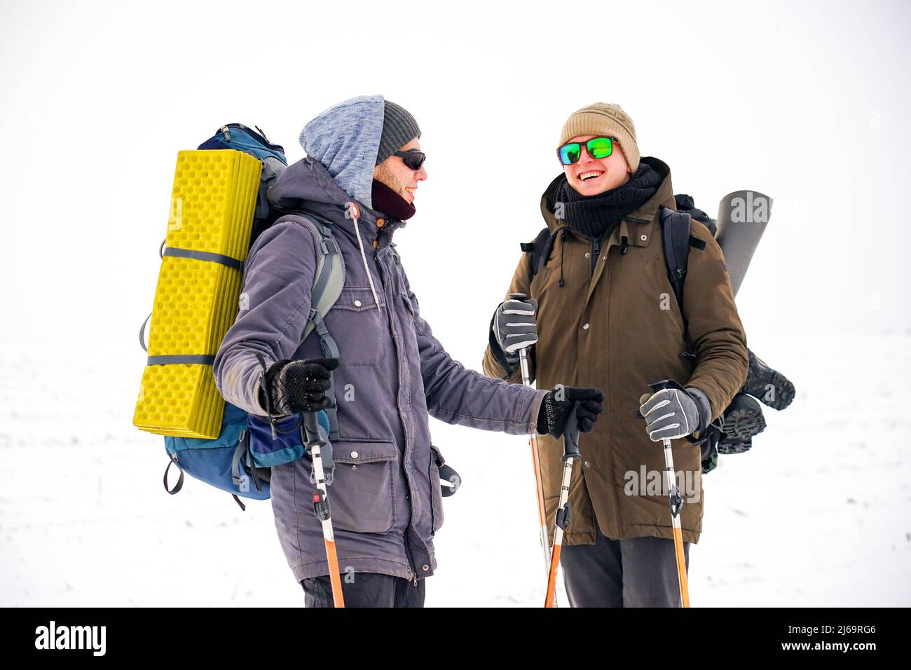 Zwei Jungs laufen während einer Winterexpedition durch lockeren Schnee. Sie tragen große Rucksäcke, warme Jacken. Sie halten Trekkingstöcke in ihren Händen. Stockfoto