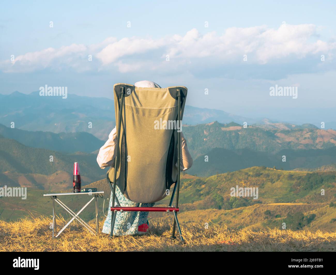 Eine Frau, die auf dem Campingstuhl am Aussichtspunkt der Berge sitzt Stockfoto