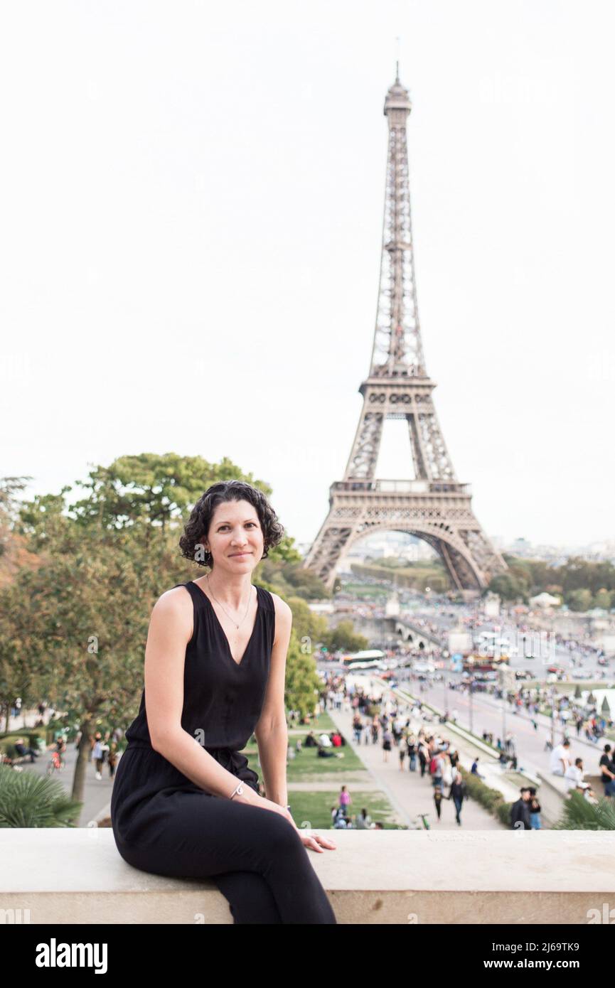 Weibliche Touristin in schwarzem Jumpsuit lächelnd vor dem Eiffelturm Stockfoto