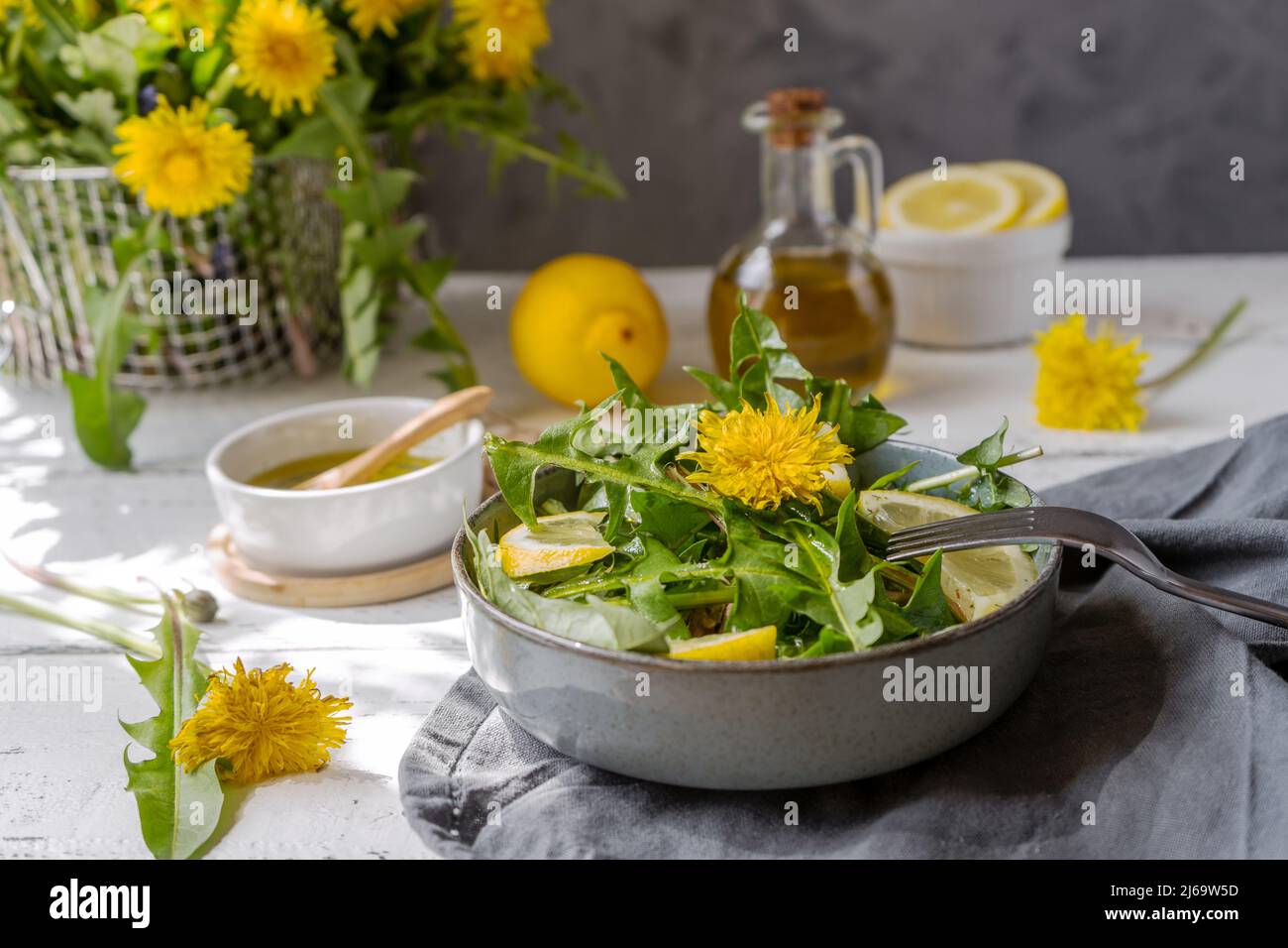 Dandelionensalat mit Olivenöl, Zitronensaft und Gewürzen auf weißem Holztisch mit grauem Hintergrund Stockfoto