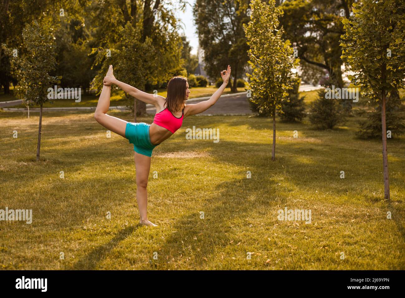 Attraktive Frau, die Yoga praktiziert. Schöne junge Brünette führt Stretching in der Übung Natarajasana, Pose des Herrn des Tanzes, Training in der Natur Stockfoto