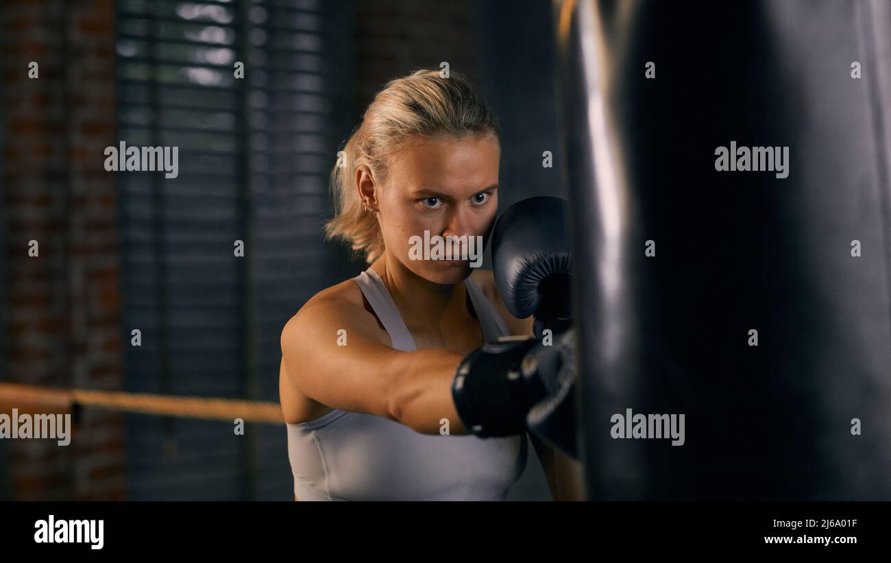 Horizontales Porträt einer starken Frau, die während des Boxtrainings einen schweren Beutel trifft Stockfoto