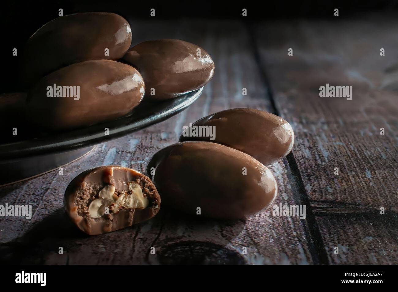 Milchschokolade überzogene Nüsse auf einem schwarzen Teller und über einem rustikalen Holztisch Makro dunkle Lebensmittel Fotografie horizontale Seitenansicht aufgenommen Stockfoto