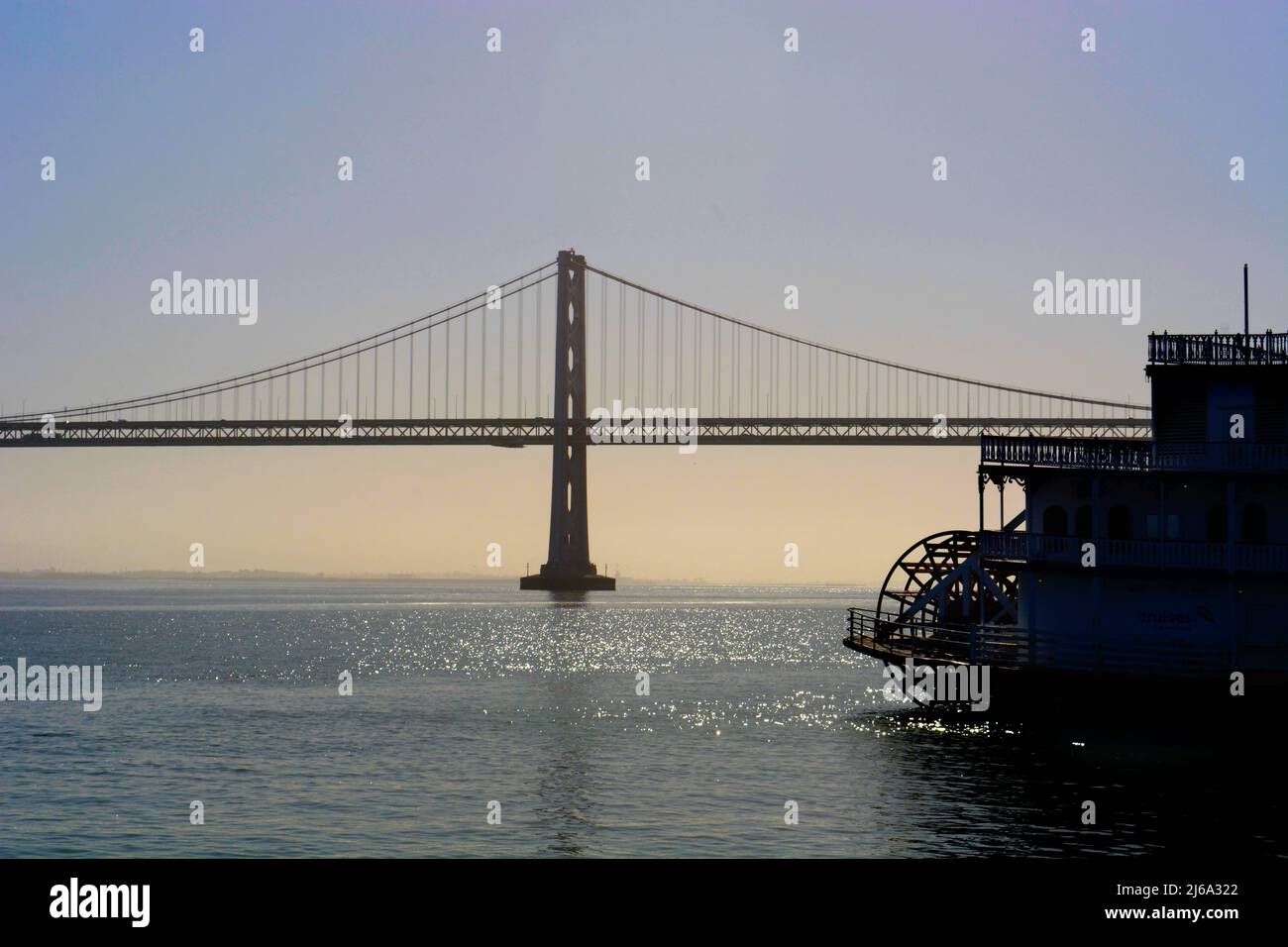 Die San Francisco-Oakland Bay Bridge und ein Tretboot für Touristen werden in San Francisco, Kalifornien, gegen die Nachmittagssonne geschildet. Stockfoto