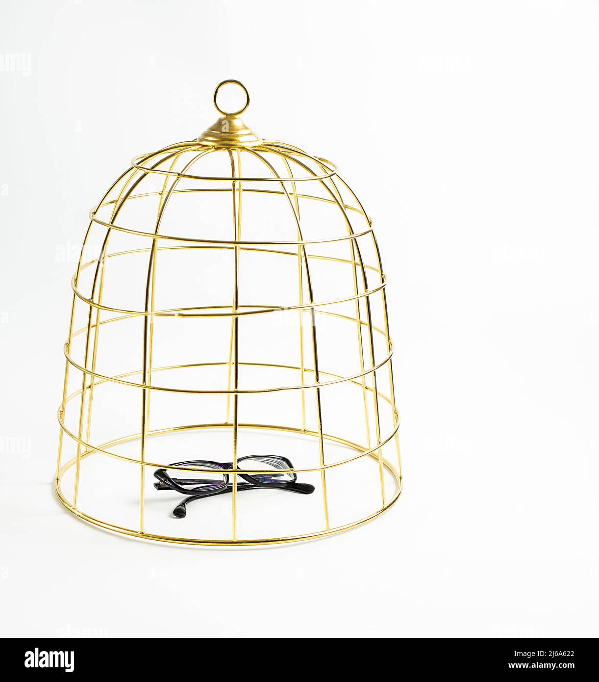 Großer goldener Vogelkäfig und schwarze Gläser auf weißem Hintergrund, Konzept, Stock Foto Stockfoto