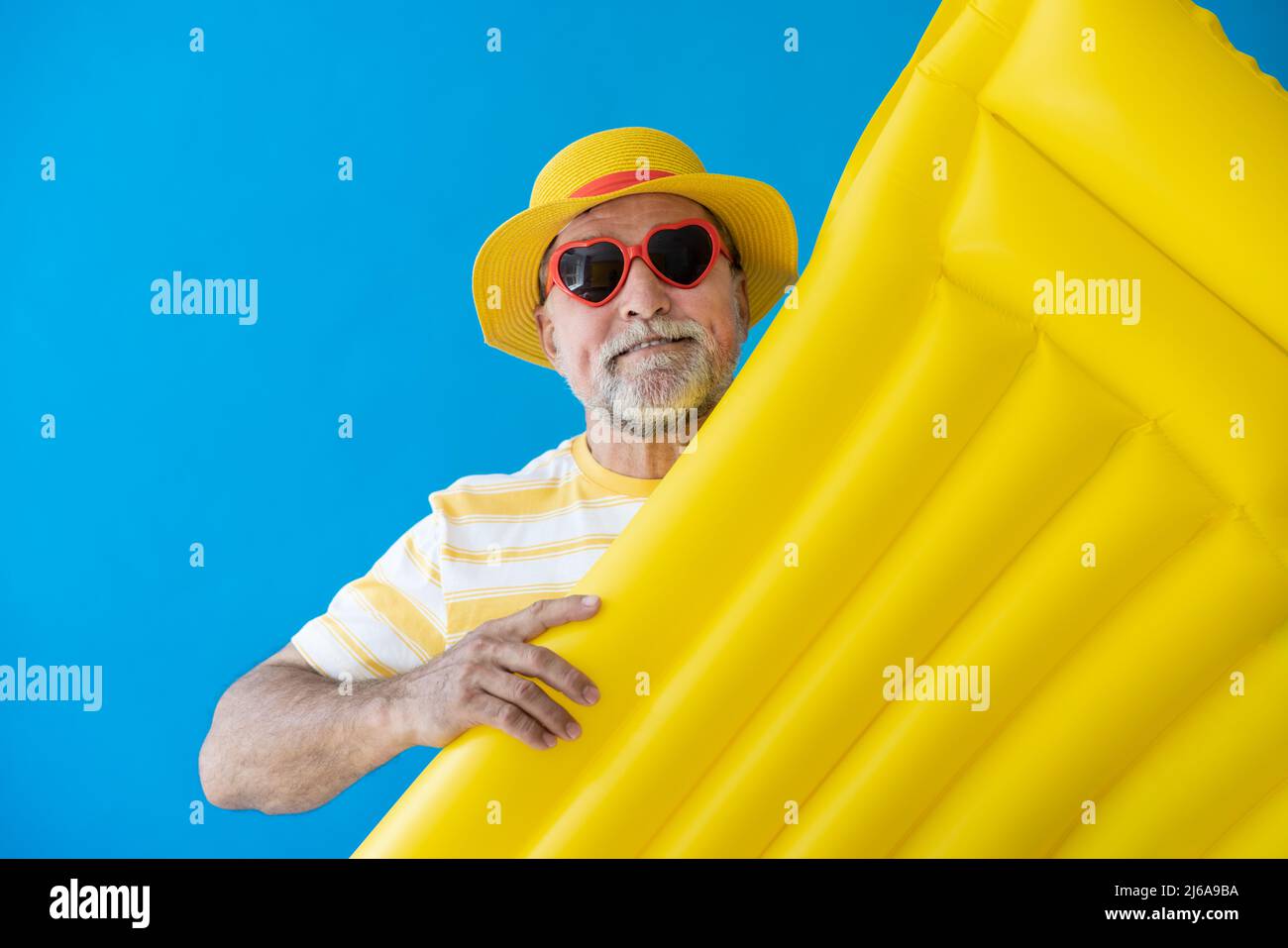 Glücklicher älterer Mann, bereit zu reisen. Person mit gelber Luftmatratze. Sommerurlaub und Urlaubskonzept Stockfoto