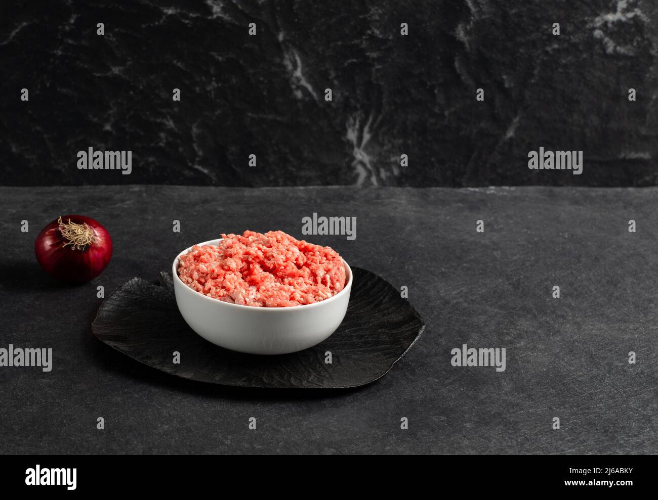 Teller mit frisch gemahlenem Rindfleisch, roter Zwiebel auf grauschwarzem Hintergrund, Platz für Text, Stockfoto Stockfoto