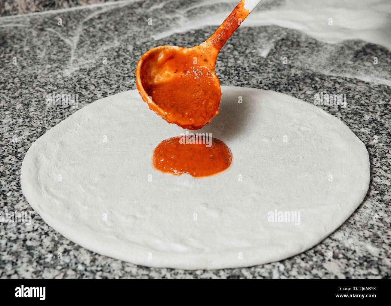 Der Koch gießt Tomatensauce über den gerollten Teig, Restaurantkonzept, den Prozess der Zubereitung italienischer Pizza Stockfoto