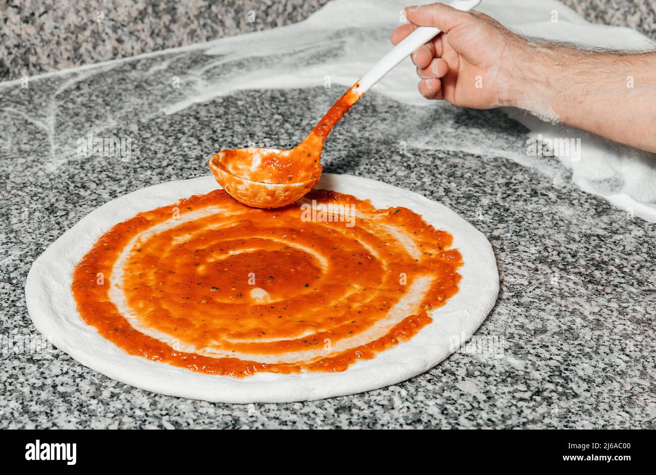 Der Koch gießt Tomatensauce über den gerollten Teig, Restaurantkonzept, den Prozess der Zubereitung italienischer Pizza Stockfoto