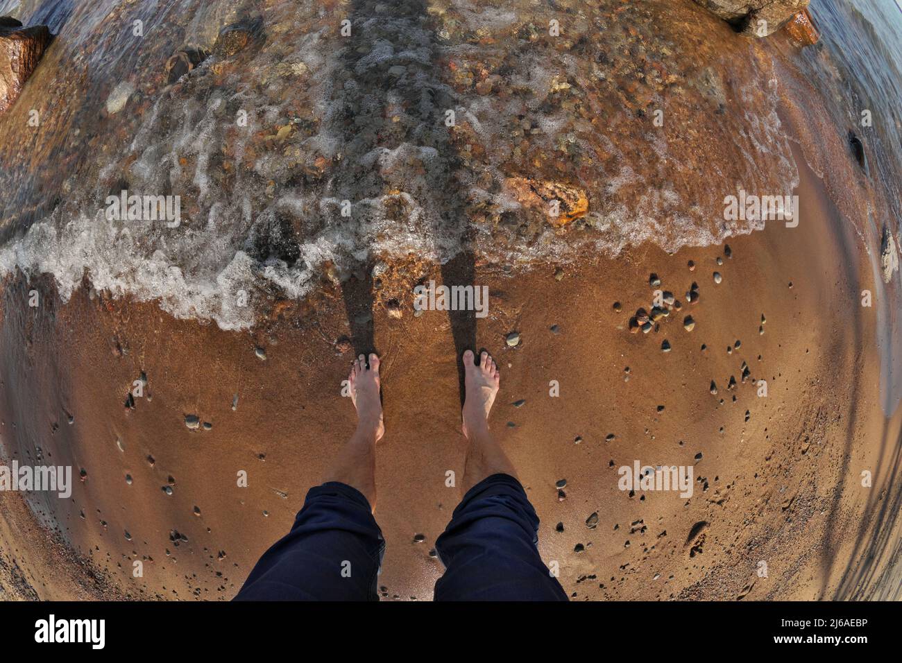 First Person Fisheye-Perspektive von Menschenfüßen im seichten Wasser mit Wellen, die in Sandy Beach Rollen Stockfoto