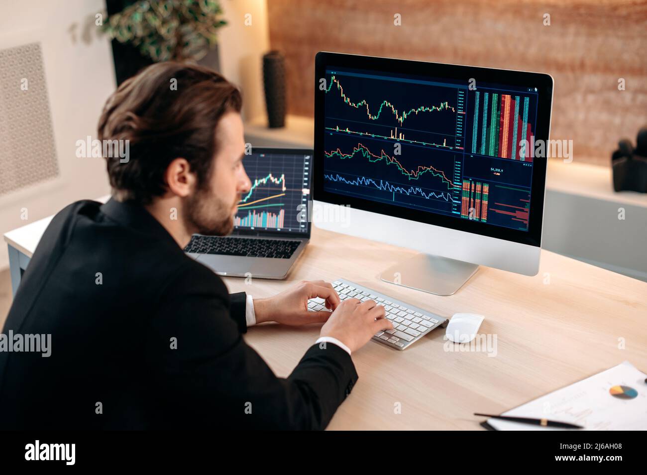 Investitionen, Handel an der Börse. Der erfolgreiche kaukasische männliche Trader-Investor, der den Kryptowährungsfinanzmarkt analysiert, schaut sich den Computer an, erarbeitet eine Krypto-Strategie und analysiert Risiken Stockfoto