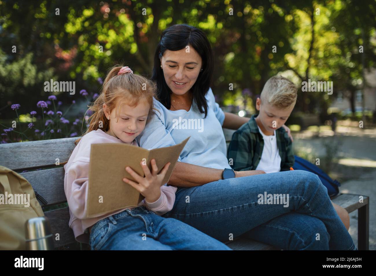 Glückliche ältere Frau mit Enkelkindern, die auf der Bank sitzen und bei Hausaufgaben im Park helfen. Stockfoto