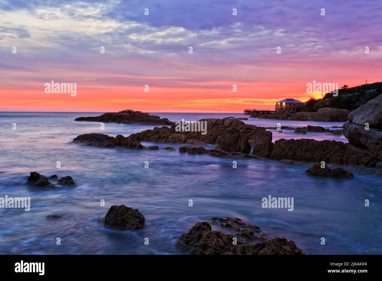 Strahlend roter Himmel im Morgengrauen über dem Kopf von Tathra mit historischem Kai vor Sandsteinfelsen - Australische Saphirküste. Stockfoto