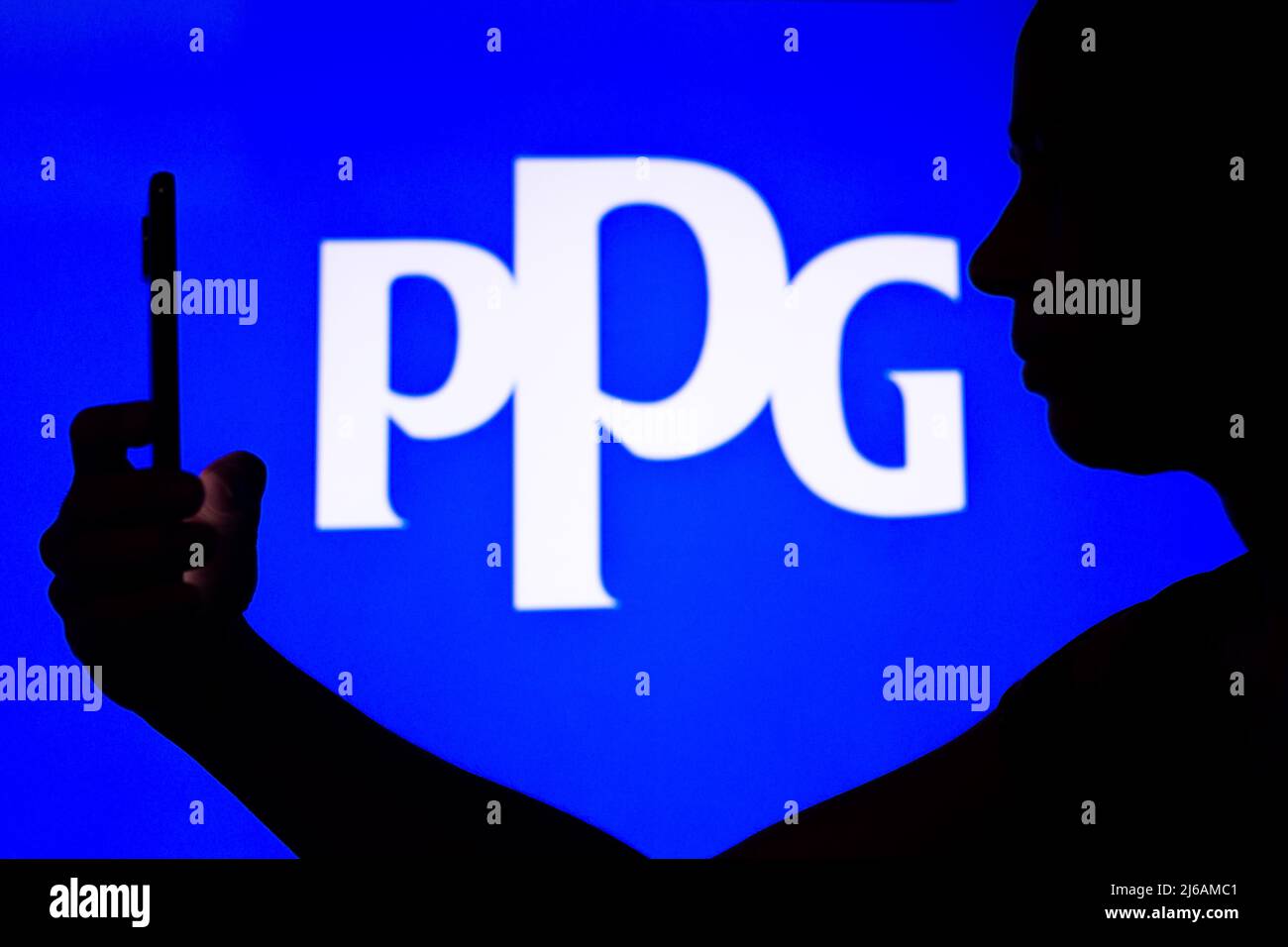 In dieser Abbildung ist das Logo von PPG Industries im Hintergrund einer Frau mit Silhouetten zu sehen, die ein Mobiltelefon in der Hand hält. Stockfoto